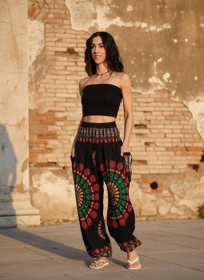 Puede incluir: Una mujer con un top de tubo negro y pantalones harem negros con un colorido dise&ntilde;o de mandala. Los pantalones tienen bolsillos y se combinan con sandalias blancas. El fondo es una pared de ladrillo desgastada.