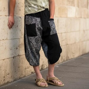 May include: Black and white patterned harem pants featuring a swirling circular design on one side and solid black fabric on the other. These loose-fitting cropped trousers include large patch pockets on the front and a comfortable elastic waistband.