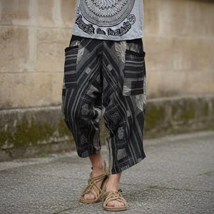 May include: Loose-fitting black and gray patterned trousers featuring a patchwork-style design with vertical stripes and geometric motifs, a wide waistband, and two large side pockets, paired with beige woven rope sandals.