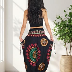 Puede incluir: Pantalones harem negros con un vibrante estampado floral en rojo, amarillo y verde. Los pantalones tienen cintura con cord&oacute;n y est&aacute;n hechos de tela ligera. La modelo lleva un top corto negro. Una opci&oacute;n c&oacute;moda y elegante.