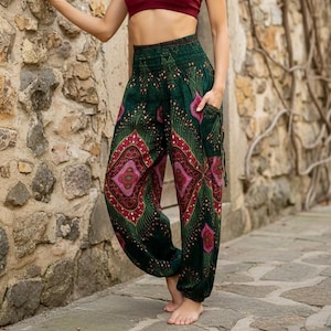 May include: Loose-fitting trousers featuring a dark green base with a repeating magenta and gold diamond-shaped pattern. The trousers have a high, smocked elastic waistband, tapered ankles, and a side pocket on the right hip with a drawstring detail.