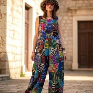 Pode incluir: Um macacão sem mangas com um design de patchwork apresentando vários padrões tie-dye em tons de azul, verde, roxo e preto. A peça tem uma silhueta solta de perna larga com tornozelos franzidos e decote quadrado. O texto diz Number 1.