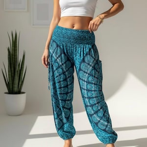 Puede incluir: Pantalones tipo harén en color azul cerceta y azul oscuro con un patrón de cachemira repetitivo, una cintura elástica fruncida ancha y tobillos elásticos. Los pantalones se combinan con un top corto sin mangas blanco y sandalias blancas.