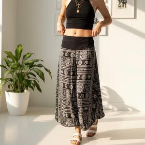 May include: A black halter top and wide-leg pants with a black and white pattern. The pants have a wide black waistband and a repeating design. The person is wearing white sandals and gold necklaces.