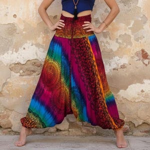 Könnte beinhalten: Haremshose mit hoher Taille und einem lebendigen, mehrfarbigen Batikmuster mit komplexen schwarzen Mandala- und Blumenmotiven. Das Kleidungsstück hat einen breiten, elastischen gesmokten Bund und eine lockere, fließende Silhouette, die an den Knöcheln schmaler wird.