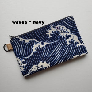 May include: A navy blue zippered pouch with a white wave pattern. The pouch has a cork zipper pull and the text "waves - navy" is printed on the front.