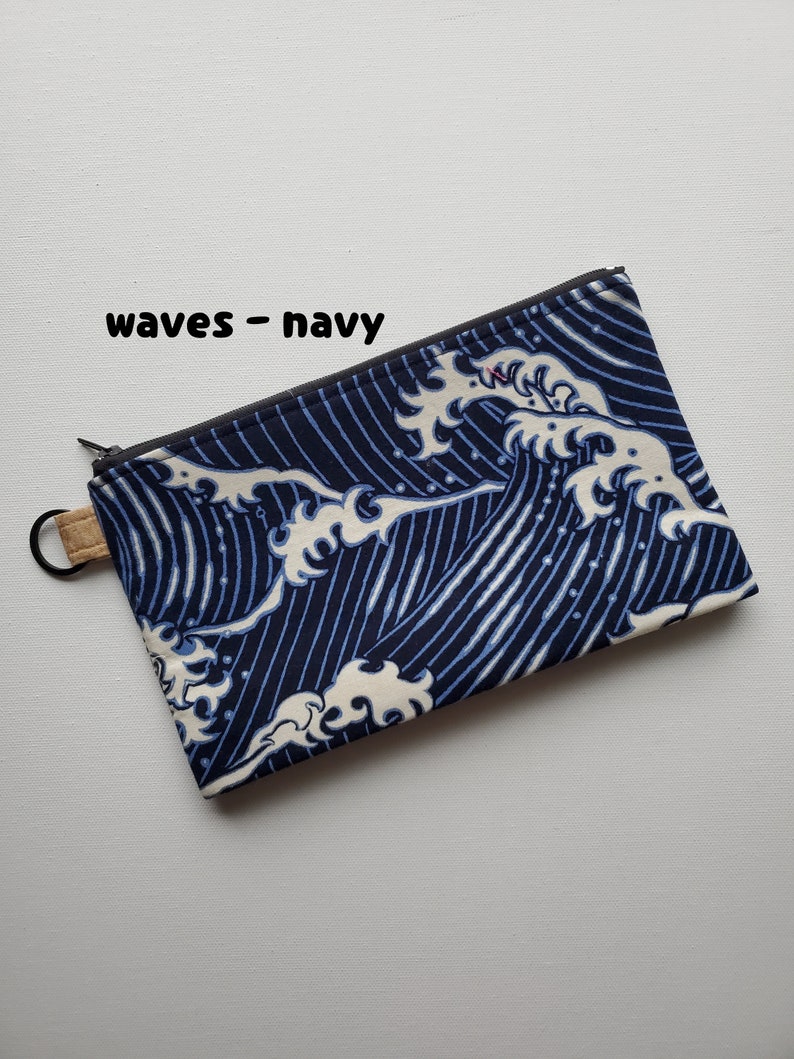 May include: A navy blue zippered pouch with a white wave pattern. The pouch has a cork zipper pull and the text "waves - navy" is printed on the front.