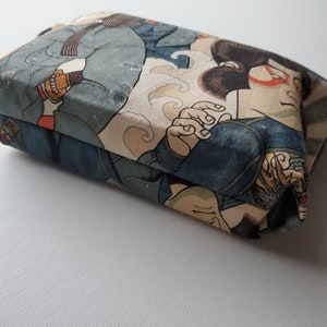 May include: A small, rectangular pouch with a Japanese-inspired print featuring figures in blue and beige clothing. The pouch is made of fabric and has a zipper closure.
