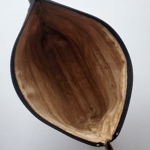 May include: A brown zippered pouch with a black zipper and a brown lining. The pouch is open and the lining is visible.