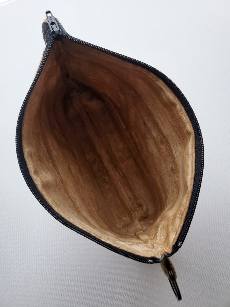 May include: A brown zippered pouch with a black zipper and a brown lining. The pouch is open and the lining is visible.