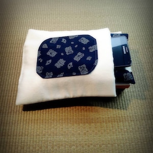 May include: A white pillow with a blue pocket featuring a repeating pattern of small white animals. A black cell phone is in the pocket.