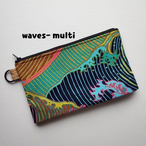 May include: A zippered pouch with a colourful wave pattern in shades of blue, green, yellow, pink, and brown. The pouch has a black zipper and a brown strap.