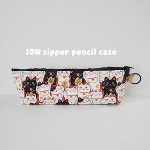 May include: A rectangular pencil case with a black zipper and a loop. The case is white with a repeating pattern of black, white, and gold Japanese lucky cats. The text "10W zipper pencil case" is printed on the front.