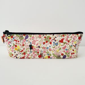 May include: A white zippered pencil case with a floral print featuring small red, pink, yellow, and purple flowers, green leaves, and small black and white cats.