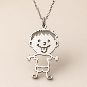 Op de afbeelding: Een zilverkleurige metalen ketting met een hanger in de vorm van een uitgesneden silhouet van een kind met een lachend gezicht, tong uitgestoken, gekleed in een t-shirt en korte broek. De hanger hangt aan een fijne, bijpassende schakelketting.