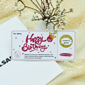 Puede incluir: Una tarjeta de felicitación de cumpleaños con las palabras "Happy Birthday" en cursiva. La tarjeta incluye un área para rascar que dice "A ticket to Hawaii". La tarjeta está decorada con estrellas y una corona.