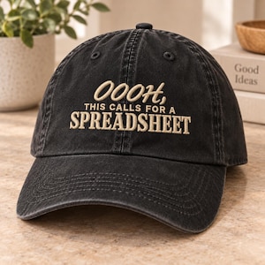 May include: A black baseball cap with a washed-out finish featuring the embroidered text in a light tan color that reads: OOOH, THIS CALLS FOR A SPREADSHEET. The cap has a curved brim, a button on the top, and stitched eyelets for ventilation.