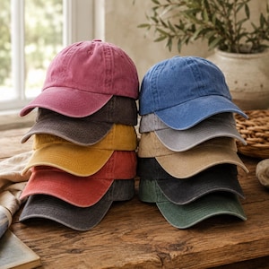 May include: A stack of two columns of baseball caps in various colors including pink, dark gray, yellow, red, charcoal, blue, light gray, tan, black, and green. Each cap features a curved brim and a six-panel construction with a button on top.