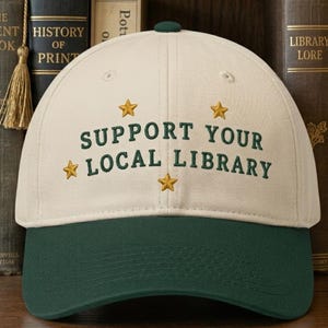 Peut inclure: Casquette de baseball avec une couronne crème et une visière vert foncé. Le texte brodé "SUPPORT YOUR LOCAL LIBRARY" est orné d'étoiles dorées. Bouton vert foncé sur le dessus.