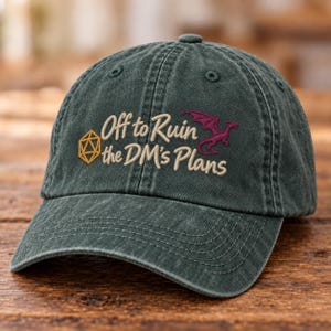 May include: A dark green baseball cap with a distressed finish. The front features embroidered text that reads Off to Ruin the DM's Plans in a light tan script. To the left is a yellow twenty-sided die and to the right is a small purple dragon.