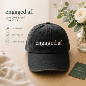 May include: A dark grey baseball cap with the words "engaged af" embroidered in white. The cap is made from 100% cotton and has an adjustable fit. The image also includes the text "Your love story, your style."
