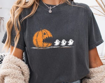 May include: Dark grey t-shirt featuring a Halloween-themed graphic. The design includes an orange pumpkin with a carved-out mouth and three white ghost figures. The shirt is made of a soft material.