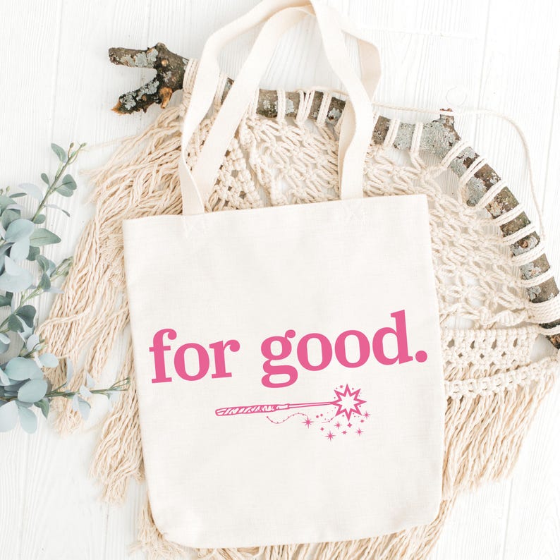 May include: Cream-colored tote bag with the phrase "for good." in bright pink lettering. Below the text is a pink illustration of a magic wand with stars. The bag has two cream-colored handles.