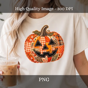 May include: A cream-coloured t-shirt featuring a large, central graphic of a jack-o'-lantern pumpkin. The pumpkin is designed with a patchwork pattern of orange, brown, and white fabrics, including plaid, floral, and leopard prints, with black eyes and mouth.