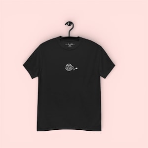 May include: Black t-shirt with a white brain graphic and a cord design. The shirt is hanging on a black hanger against a light pink background. The graphic is a simple line drawing of a brain with a cord attached.