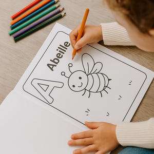 K&ouml;nnte beinhalten: Ein Kind malt eine Seite in einem Malbuch mit dem Wort "Abeille" und einer Cartoon-Biene aus. Das Kind benutzt einen orangefarbenen Buntstift. Mehrere Buntstifte sind sichtbar.