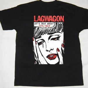 以下が含まれることがあります： 黒いTシャツ。泣いている女性のポップアート風イラストで、赤い唇と爪が特徴です。Tシャツには、画像の上に赤いブロック文字でバンド名「LAGWAGON」があり、「LET'S TALK ABOUT FEELINGS」というフレーズが吹き出しの中にあります。