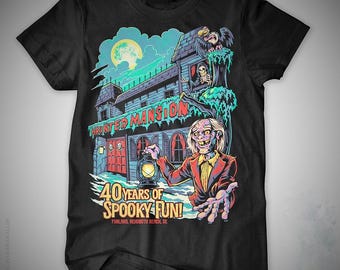 Könnte beinhalten: Schwarzes T-Shirt mit einem farbenfrohen Grafikdesign eines Spukhauses und einem Zombie mit einer Laterne. Der Aufdruck enthält den Text "HAUNTED MANSION" und "40 YEARS OF SPOOKY FUN!"
