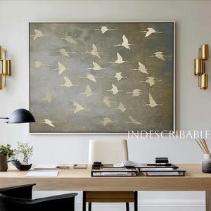 May include: A modern office space featuring a large abstract painting of flying birds in gold and gray tones. The room includes a wooden desk, black chair, and gold light fixtures. The text "INDESCRIBABLEBEAUTY" is visible.