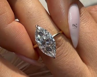 Könnte beinhalten: Ein goldener Ring mit einem Diamanten im Marquiseschliff. Der Diamant ist klar und reflektiert das Licht. Der Ring befindet sich an einem Finger mit einem hellrosa Nagel. Das Bild enthält den Text "BN Fine Jewelry".