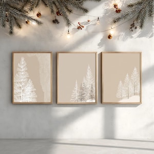 Könnte beinhalten: Drei gerahmte Kunstdrucke mit minimalistischen Illustrationen von Winterbäumen in Weiß und Grau vor beigem Hintergrund. Das Kunstwerk wird an einer weißen Wand mit festlichen Lichtern und Grün in der Hintergrund gezeigt.