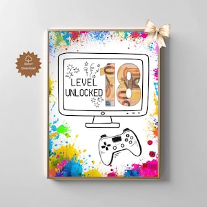 May include: A framed print with a gold border, featuring a black and white illustration of a computer monitor and a game controller. The monitor displays the text "LEVEL UNLOCKED" and the number "18". Colorful paint splatters surround the image.