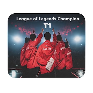 Può includere: Un tappetino per mouse con l'immagine di una squadra in giacche rosse che celebra una vittoria. Il testo "League of Legends Champion" e "T1" sono visualizzati in alto. I giocatori puntano verso l'alto. Il nome "FAKER" è visibile su una giacca.