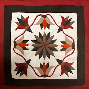 May include: A white fabric square with a brown border and a repeating pattern of stylized flowers in shades of brown, red, and beige.