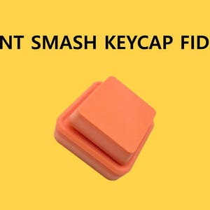 May include: Orange giant keycap fidget toy on a yellow background. The text "GIANT SMASH KEYCAP FIDGET" is displayed above the toy. The fidget toy is square and has a smaller square on top of a larger square.