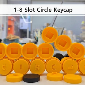May include: Yellow and black keycaps arranged to spell "CIRCLE". The keycaps have a circular design with a square center. The text "1-8 Slot Circle Keycap" is displayed at the top of the image. The keycaps are on a white surface.