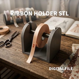 Op de afbeelding: Een donkergrijze lintenhouder met een centrale stang die een spoel met licht perzikkleurig lint vasthoudt. De tekst RIBBON HOLDER STL en DIGITAL FILE is zichtbaar. De houder heeft een U-vormig frame om de spoel gemakkelijk af te rollen.