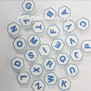 May include: White hexagonal keycaps with blue outlines and letters. The keycaps are scattered across a white surface. The text "HEX-Outline Keycaps" is visible in the image.