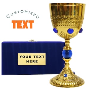 Może przedstawiać: Złoty kielich z niebieskimi akcentami i pasującym niebieskim aksamitnym pudełkiem. Kielich ma skomplikowane detale i niebieskie kamienie szlachetne. Pudełko ma złotą płytkę z napisem "YOUR TEXT HERE". Tekst "CUSTOMIZED TEXT" znajduje się nad pudełkiem.