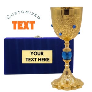 May include: A gold-colored chalice with ornate floral patterns and blue gemstone accents. The chalice is displayed with a blue velvet box that has a gold plate with the text "YOUR TEXT HERE". The image also includes the text "CUSTOMIZED TEXT".
