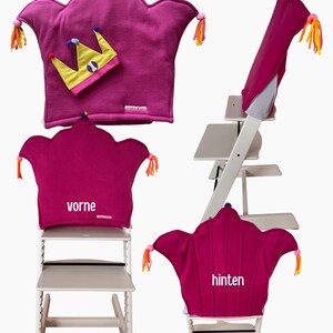 May include: A magenta crown-shaped high chair cushion with colorful tassels on the points, a small yellow crown accessory with the number one, and white text labels reading vorne and hinten on the cushion fabric.