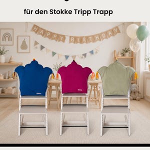 May include: Three crown-shaped high chair cushions in blue, magenta, and sage green, each featuring small colorful tassels on the sides. The cushions are designed for a wooden high chair and are displayed in a room with birthday decorations.