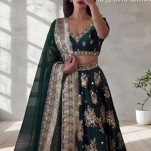 May include: A dark green, two-piece formal outfit with gold embellishments. The top has a V-neck and short sleeves. The skirt is long and flowing. A matching scarf is draped over the shoulder. The outfit is decorated with gold floral patterns. The text "Elegent fashions" is in the upper right corner.