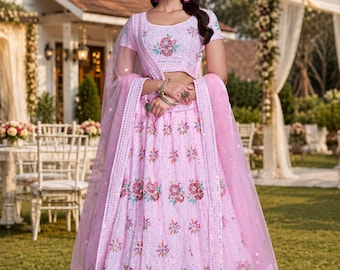May include: A light pink lehenga with floral embroidery. The set includes a short-sleeved top and a long skirt, both adorned with detailed floral patterns. A matching sheer dupatta completes the ensemble. The outfit is suitable for special occasions.