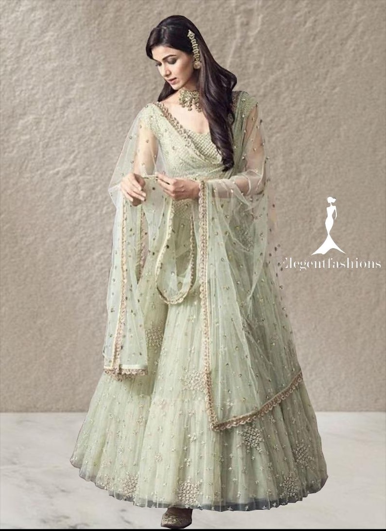 Op de afbeelding: Een lehenga choli-set in licht muntgroen met ingewikkeld borduurwerk, kralen en pailletten. Het ensemble bestaat uit een vloerlange uitlopende rok, een nauwsluitend lijfje en een transparante dupatta met een decoratieve rand. Tekst leest elegantfashions.
