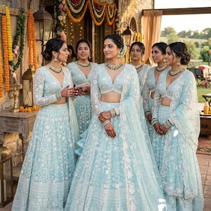 May include: A group of women in matching light blue formal dresses with intricate white floral embroidery. The dresses feature long sleeves, V-necklines, and flowing skirts. They are adorned with matching jewelry and henna designs.